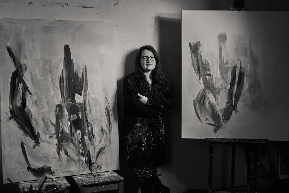 Malerin Monika Herschberger zwischen zwei ihrer Werken auf großer Leinwand